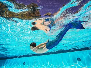 A person with a mermaid tail swims underwater in a pool, creating a magical scene.